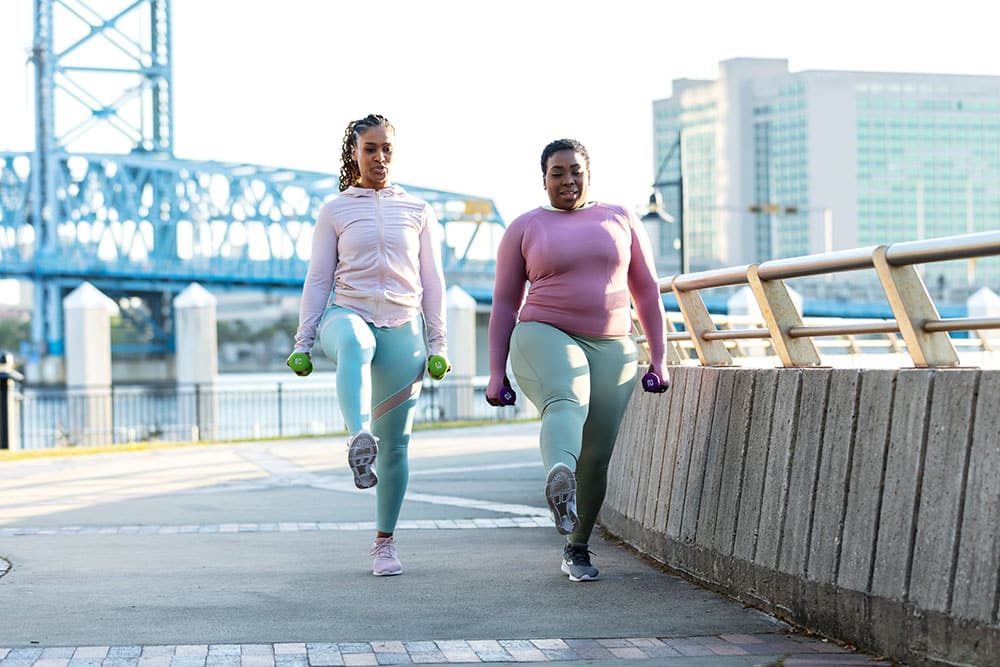 Two women performing walking lunges outside.