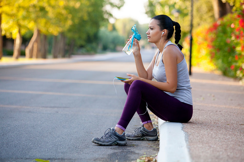 Woman sitting on sidewalk sipping water.