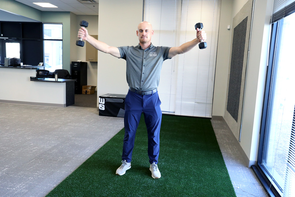 Physical Therapist performing lateral raise with dumbbells.