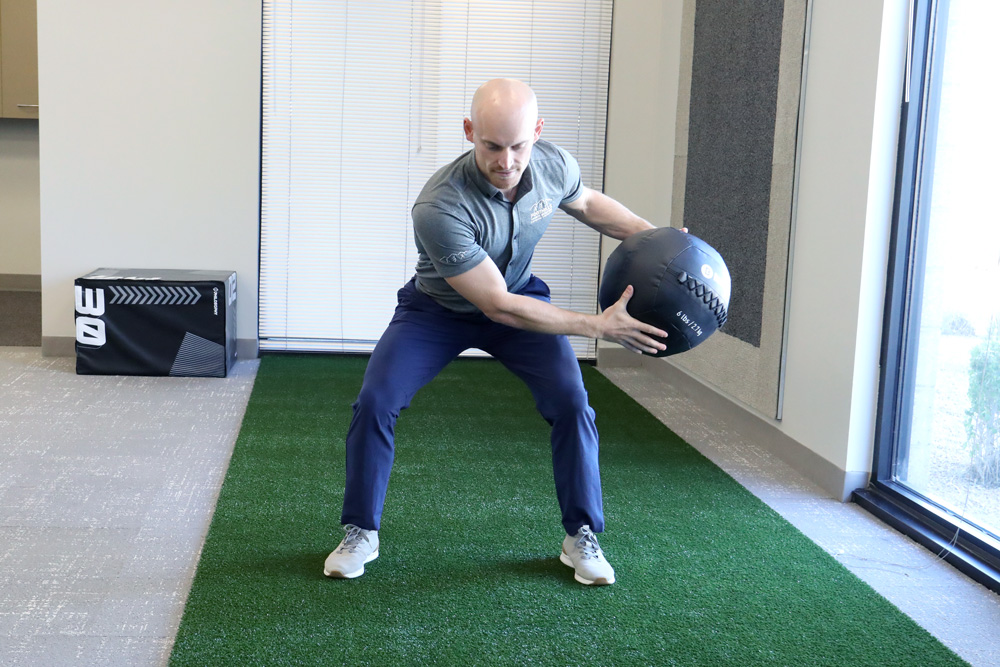 Man demonstrating wood chopper exercise with medicine ball.