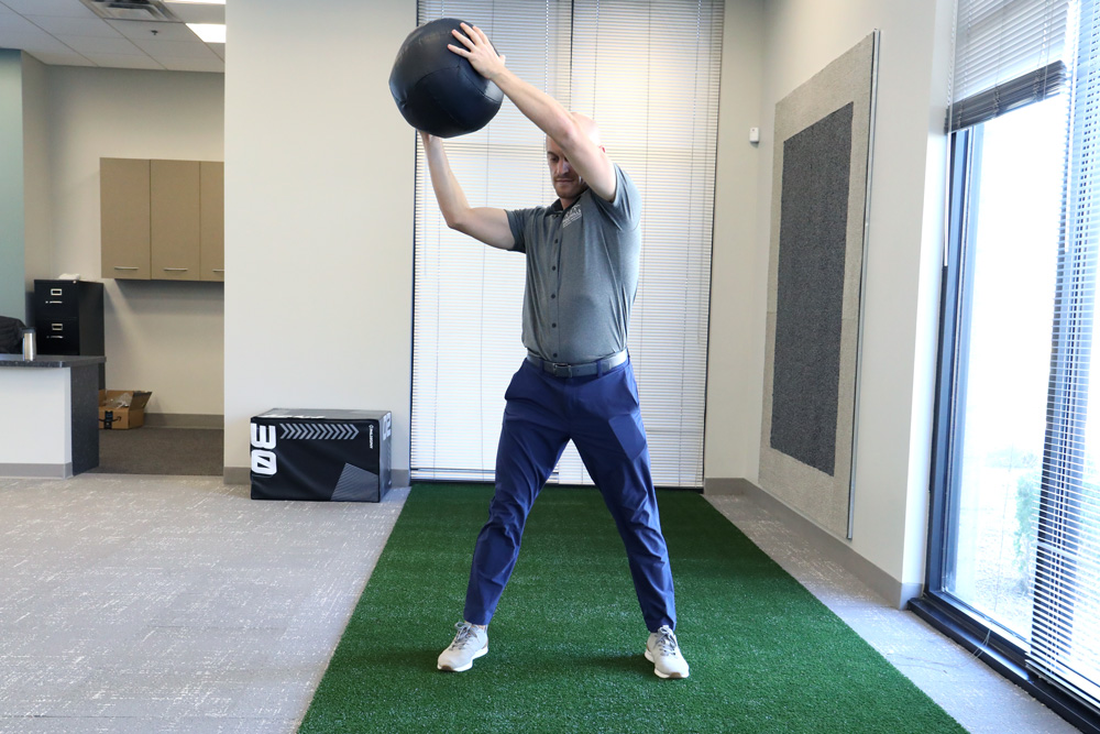 PT demonstrating wood chopper exercise with medicine ball.