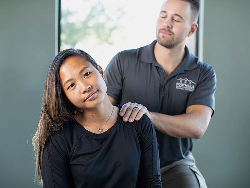 A therapist sitting behind a patient with his hand on the back of her neck