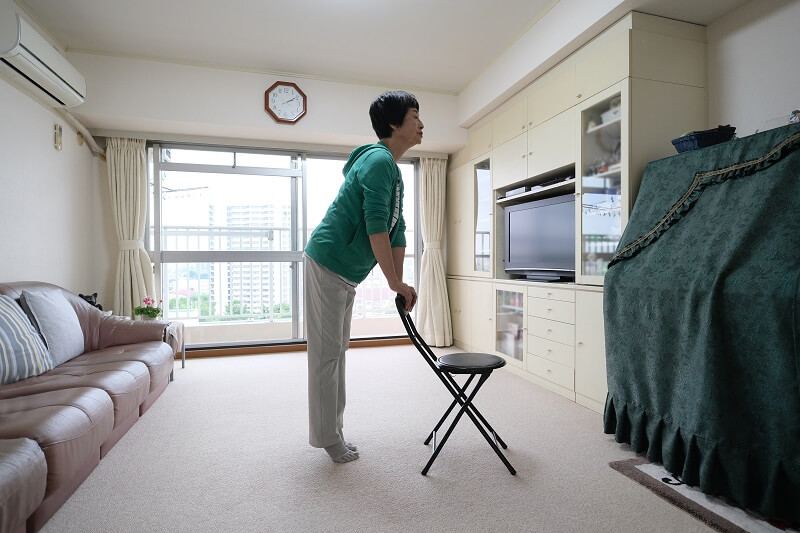 Senior female doing heel raise exercises on the back of a chair.