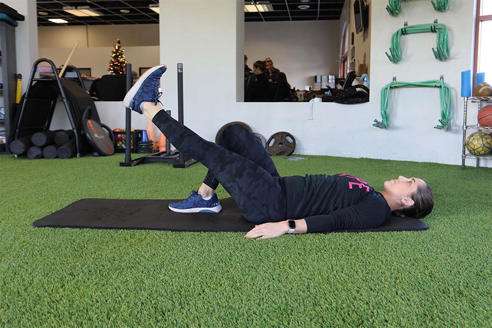 Female in a gym lying on back performing a leg exercise.