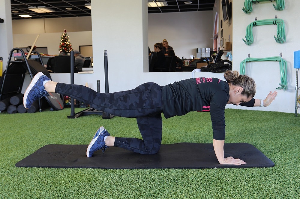 Female in a gym on a mat performing an exercise.