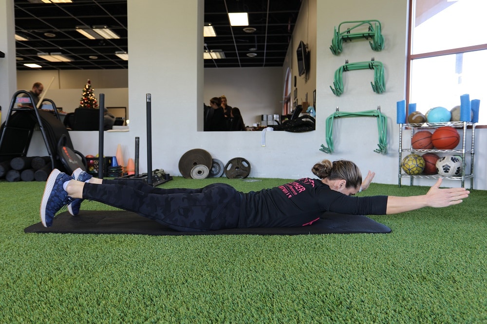 Female in a gym lying on a mat with arms stretched out.
