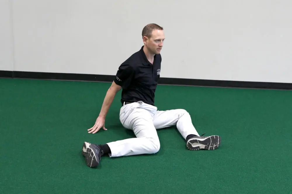 Athletic trainer stretching on gym floor.