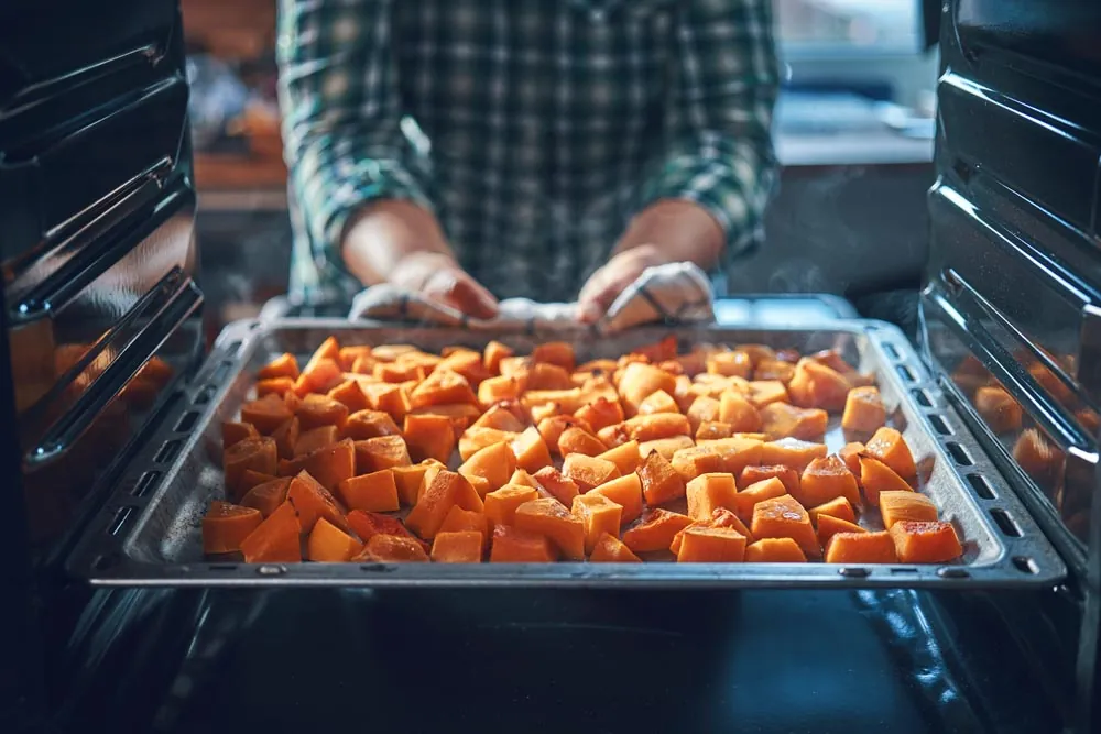 Putting chopped sweet potatos in the oven