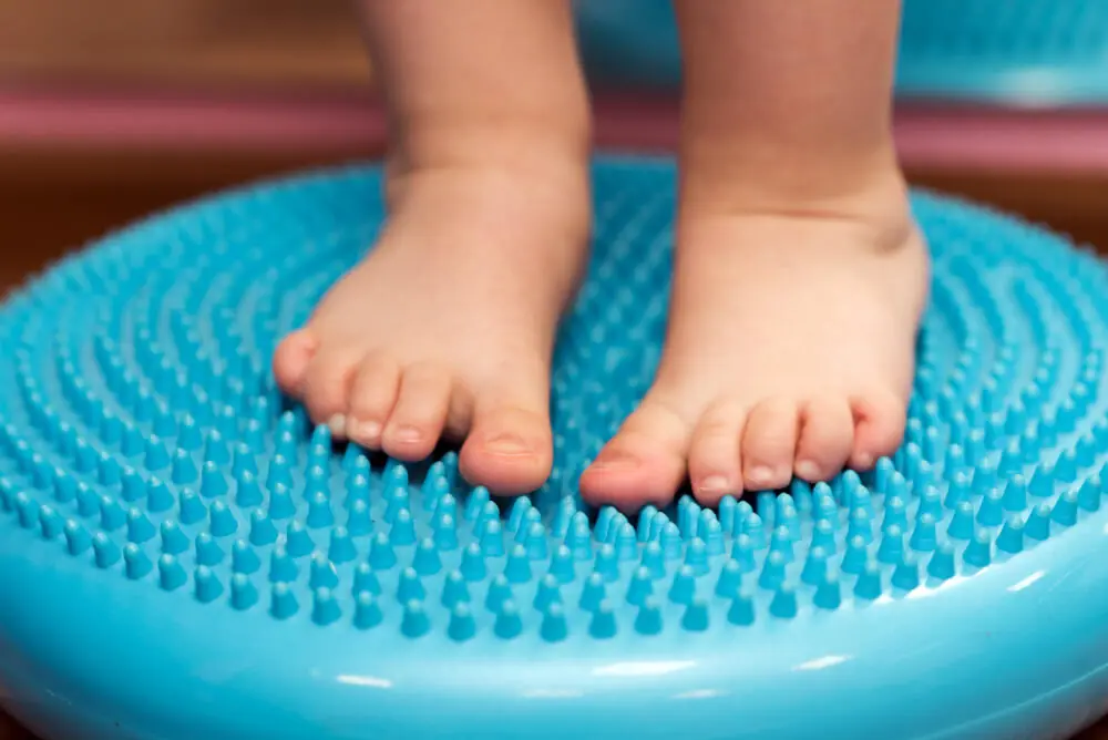 A small child massaging his feet while standing on the rug.