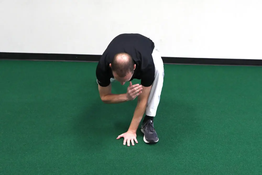Athletic trainer stretching on gym floor.
