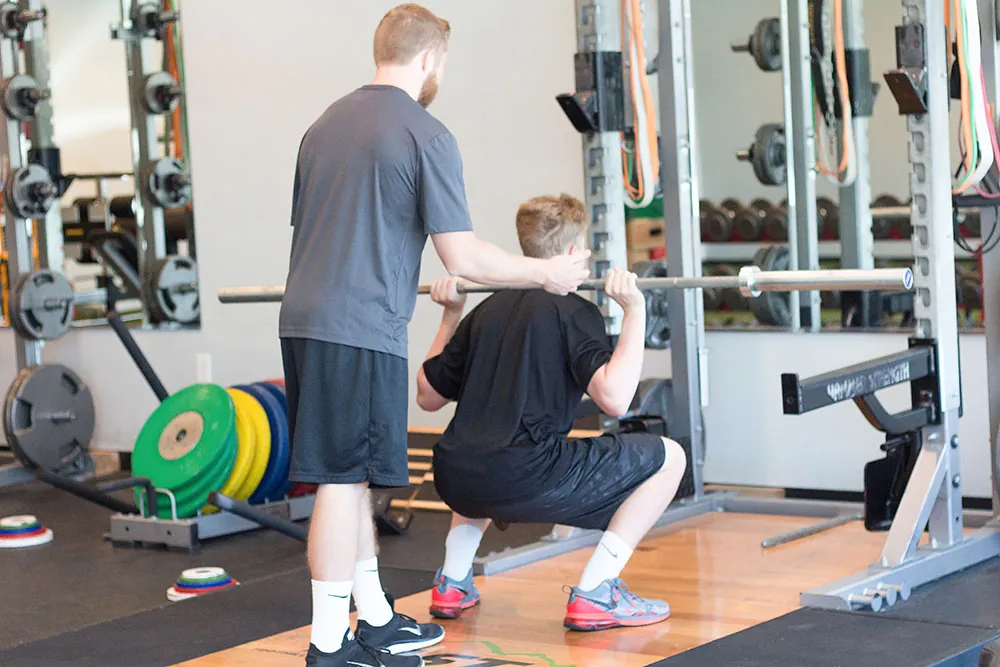 Trainer assisting young athlete in weighted squats.