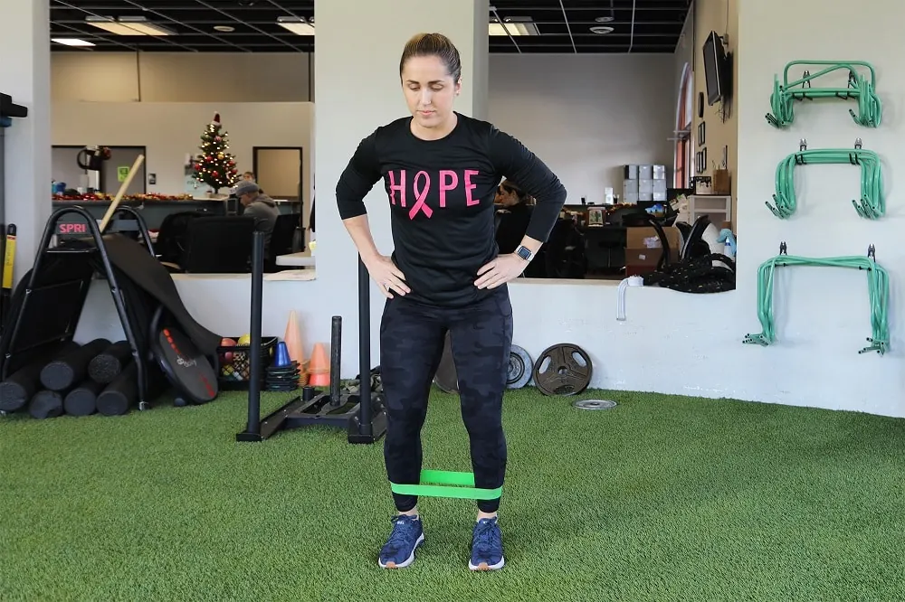 Female in a gym with arms on hips performing an exercise.