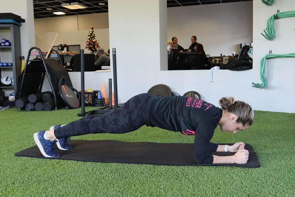 Female doing a plank on a mat in a gym.