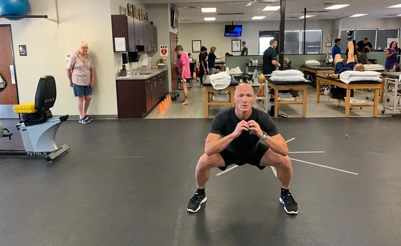 Athlete performing squat walk sidestep exercice in a gym.