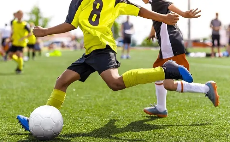 Young soccer player running fast and kicking white soccer ball.